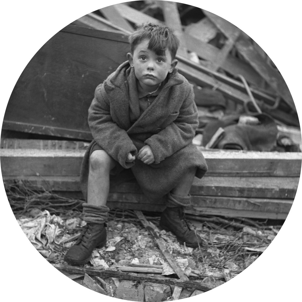 Black and white image of young boy in a coat and short pants